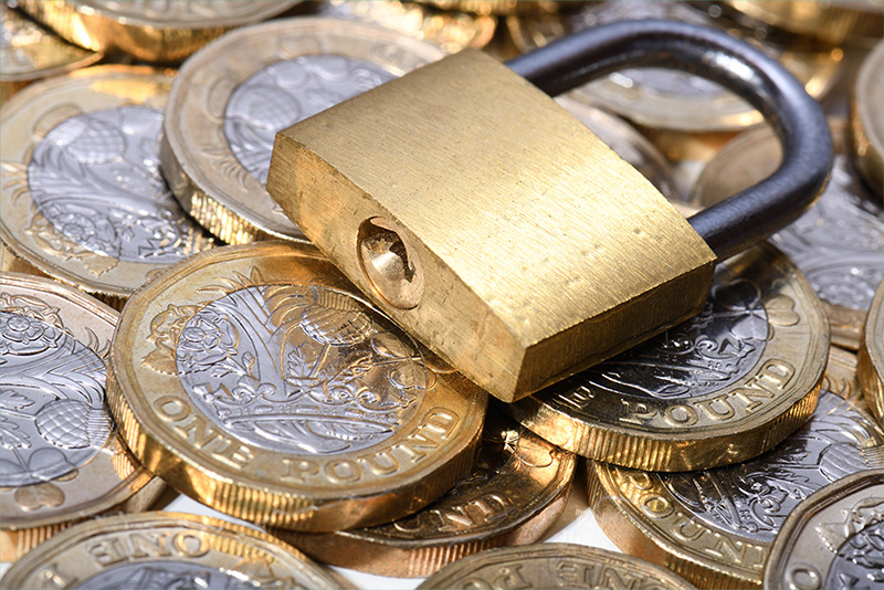 A small and shiny gold padlock lies on top of a pile of British one pound coins.